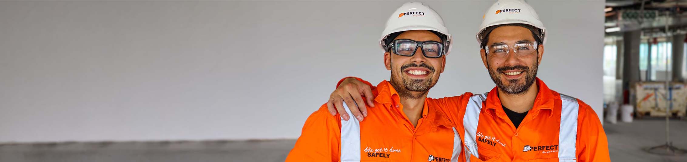 Two smiling Perfect Concrete Care workers in orange hi-vis gear and white hard hats on a concrete job site